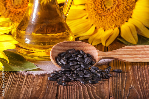 Rural still-life - the sunflower oil in glass cruet with flowers of sunflower (Helianthus annuus) and seeds in a wooden spoon, closeup
