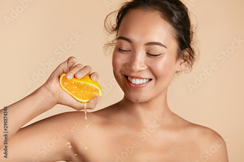 Beauty. Woman with radiant face skin squeezing orange in hand portrait. Beaut...