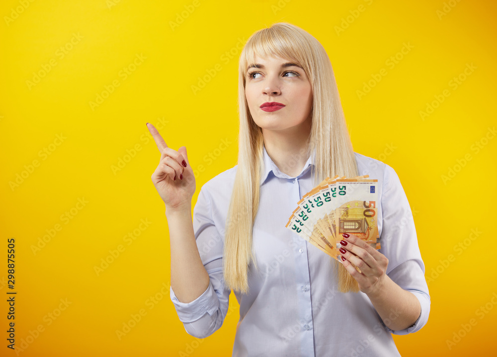 Cheerful blond woman holding money banknotes standing on a yellow background. Euro Money Banknotes Cheerful blond woman holding money banknotes standing on a yellow background. Euro Money Banknotes