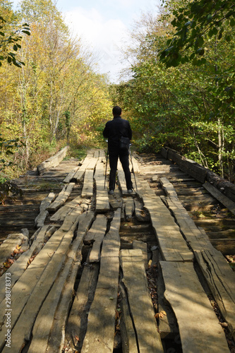 On the street is autumn. The concept of solitude in autumn day. A young man is standing in meditation on a long wooden bridge in the forest, all alone.