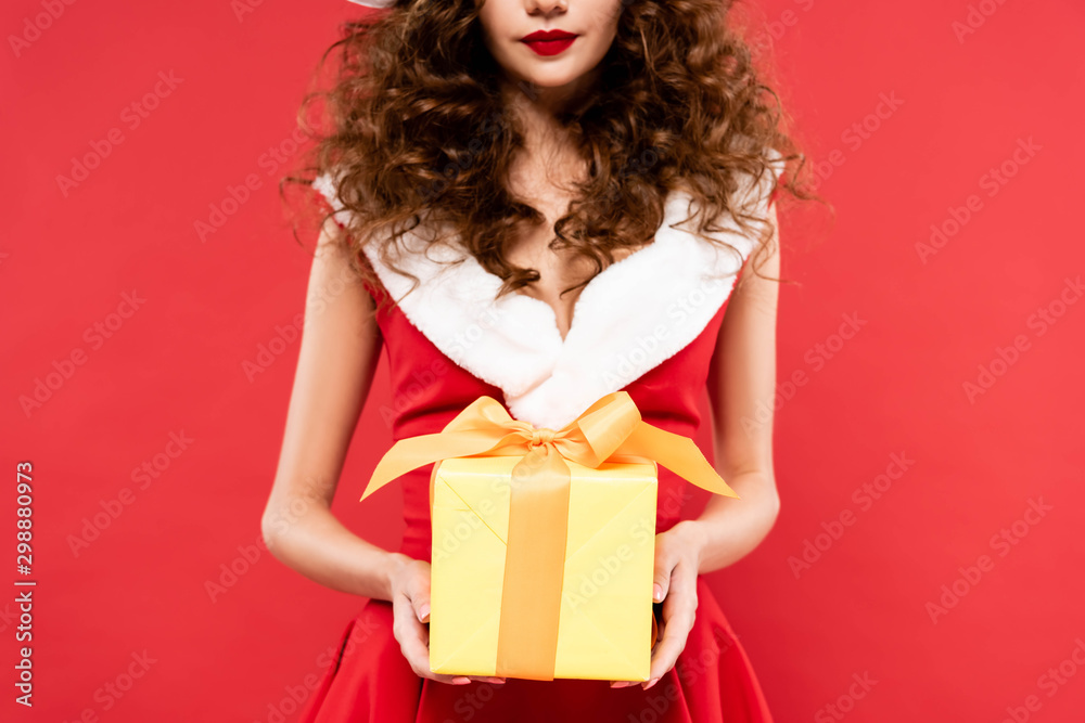 cropped view of girl in santa costume holding christmas gift, isolated on red cropped view of girl in santa costume holding christmas gift, isolated on red
