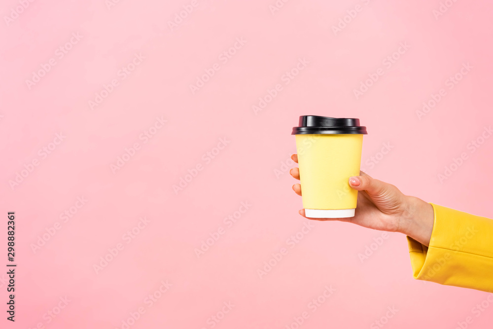 cropped view of woman holding yellow disposable cup of coffee, isolated on pink - obrazy, fototapety, plakaty 
