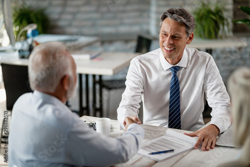 Happy financial advisor shaking hands with senior man during a meeting in the office.