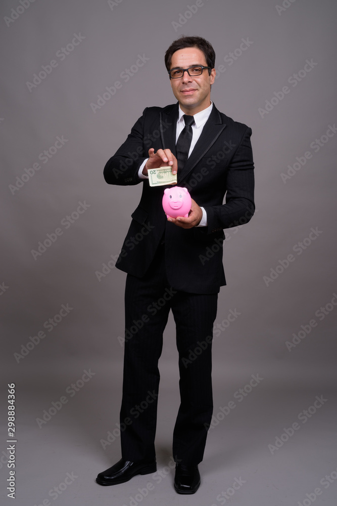 Full body shot of handsome Persian businessman with piggy bank Full body shot of handsome Persian businessman with piggy bank