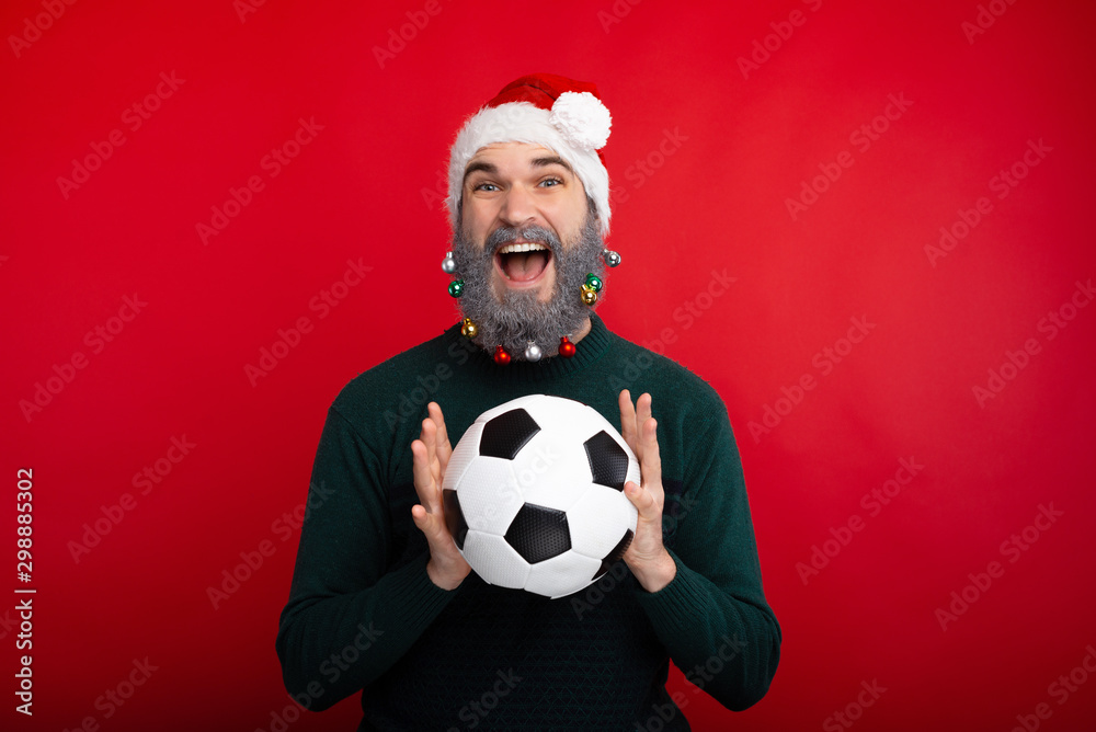 Happy smiling man with decorated beard holding soccer ball over red background Happy smiling man with decorated beard holding soccer ball over red background