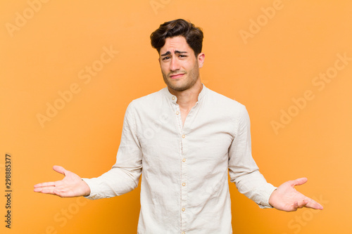 young handsome man looking puzzled, confused and stressed, wondering between different options, feeling uncertain against orange background photo