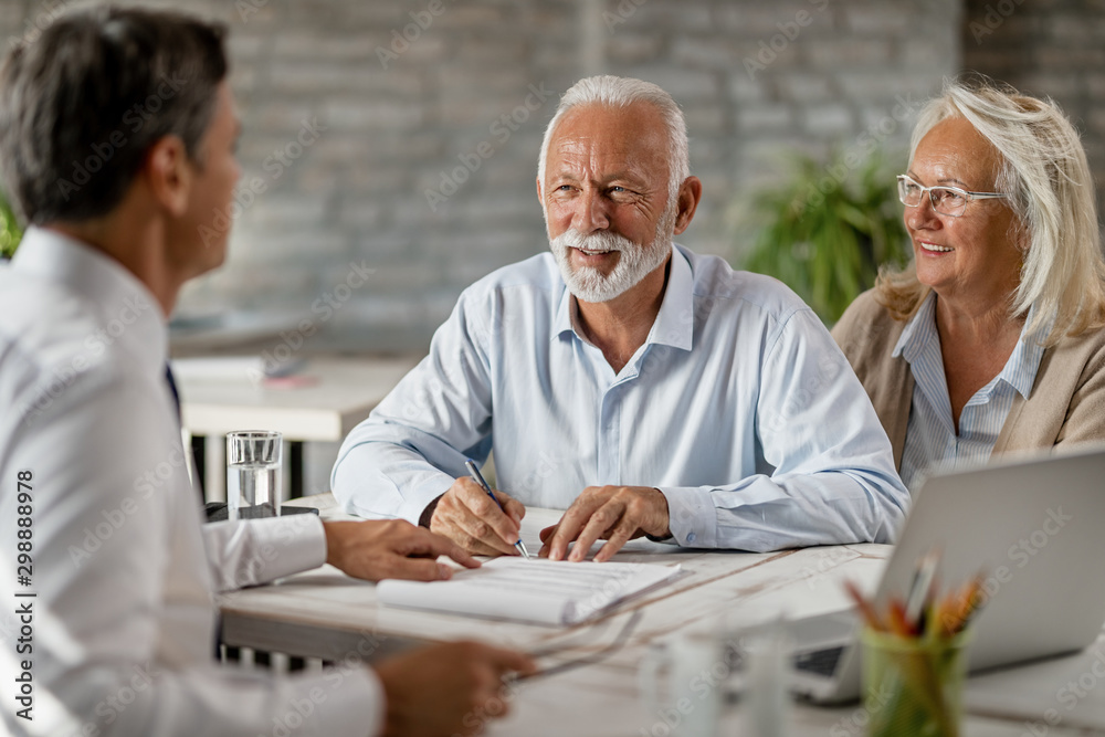 Obraz premium Happy senior couple signing an agreement while having a meeting with financial advisor.