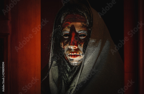 Fényképezés Creepy halloween witch with black eyes, scars on her face in a hood stands near