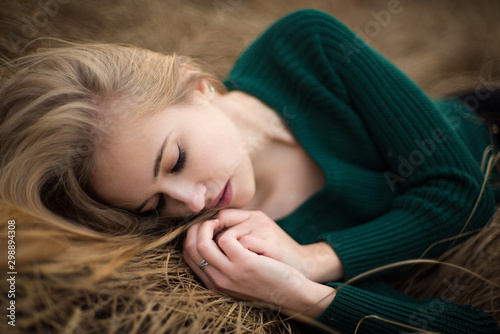 Above view of beautiful redhaired girl lying on grass, posing, embracing. Autumn forest with yellow grass. Woman with long hair, in green sweater.