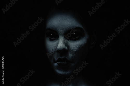 Scary and frightening  demonic woman face with black eyes in the dark.  Diabolic  and possessed by evil spirit young girl. Halloween look.