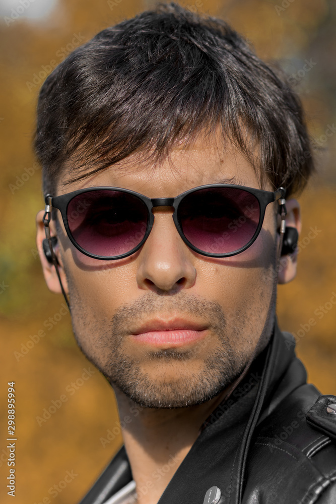 Close-up of a man's face with blurred background in sunglasses with wireless headphones Close-up of a man's face with blurred background in sunglasses with wireless headphones