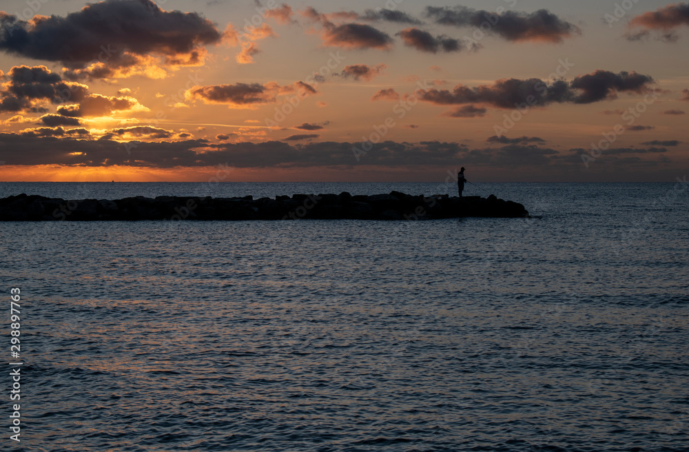 Beautiful Sunrise in Mallorca with a person fishing on the sea defences.