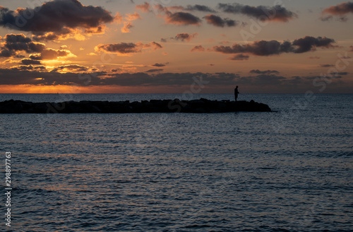 Beautiful Sunrise in Mallorca with a person fishing on the sea defences. © Geoff