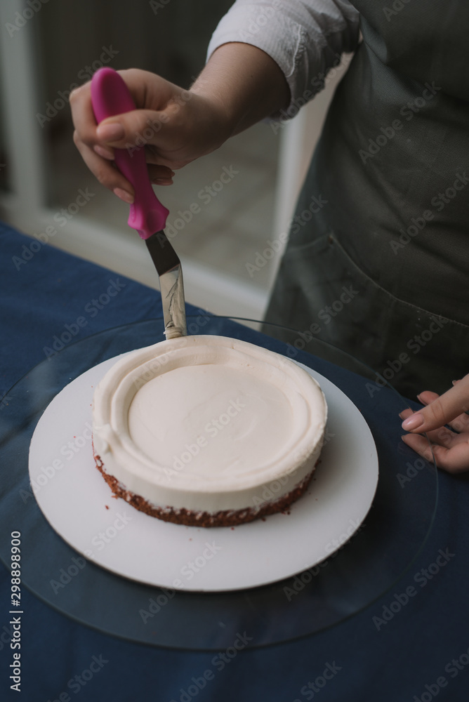 The confectioner levels the cream on the cake. The cook creates a cake, collects it and covers it with cream and then levels it with a spatula and a scraper