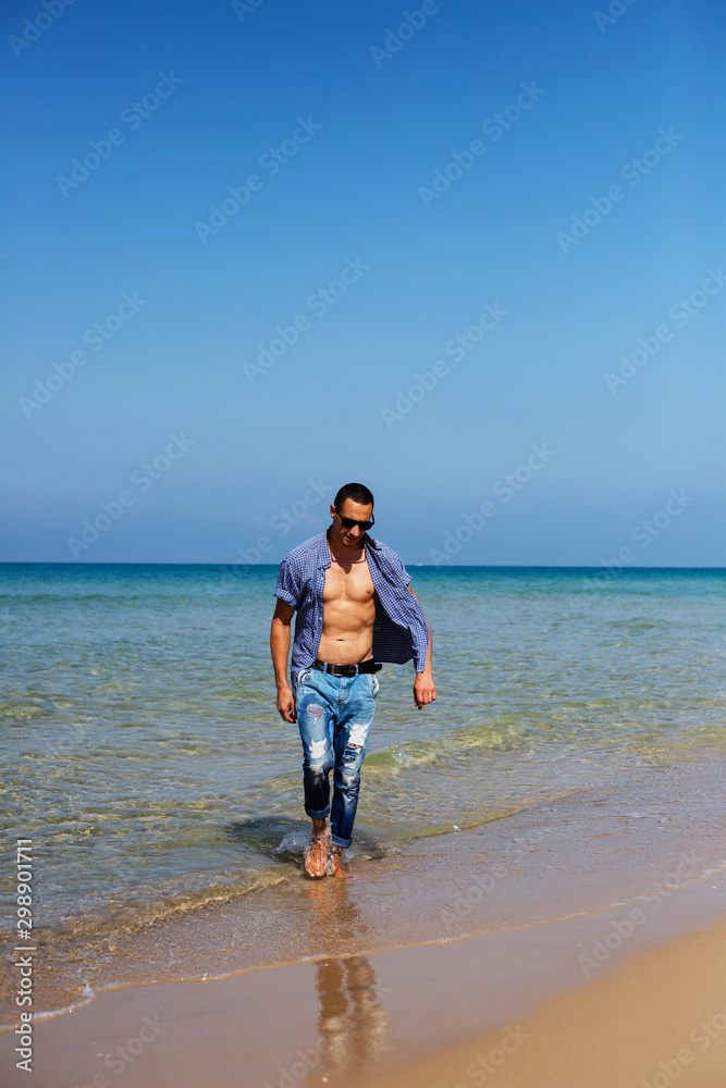 young muscular man resting and posing on the beach. A young man walks by the sea