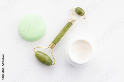 Massage roller for the face with two heads of jade stone and jar of face cream.