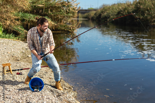 Adult man standing near river and pulling fish expressing emotions of dedication