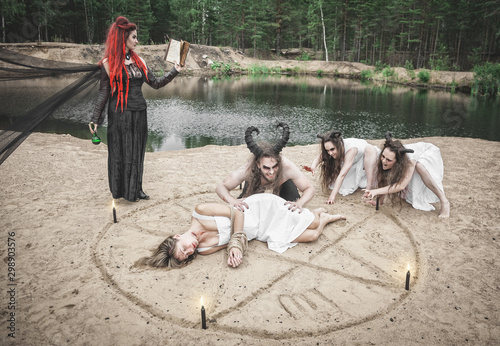 Fototapeta Beautiful witch making witchcraft with horned demons and victim