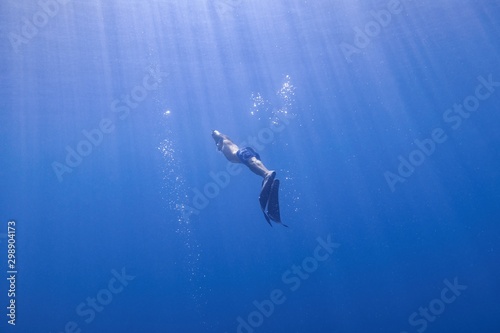 Freediver elegantly swimming from the depth to the sea surface in the shinning sunlight.