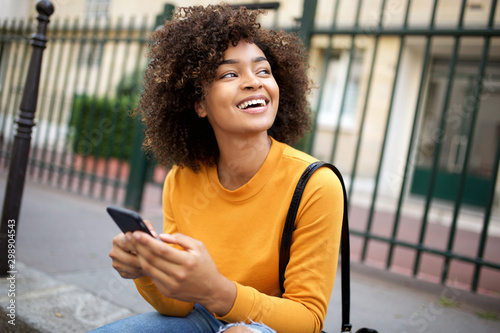 happy african american young woman holding cellphone and looking away