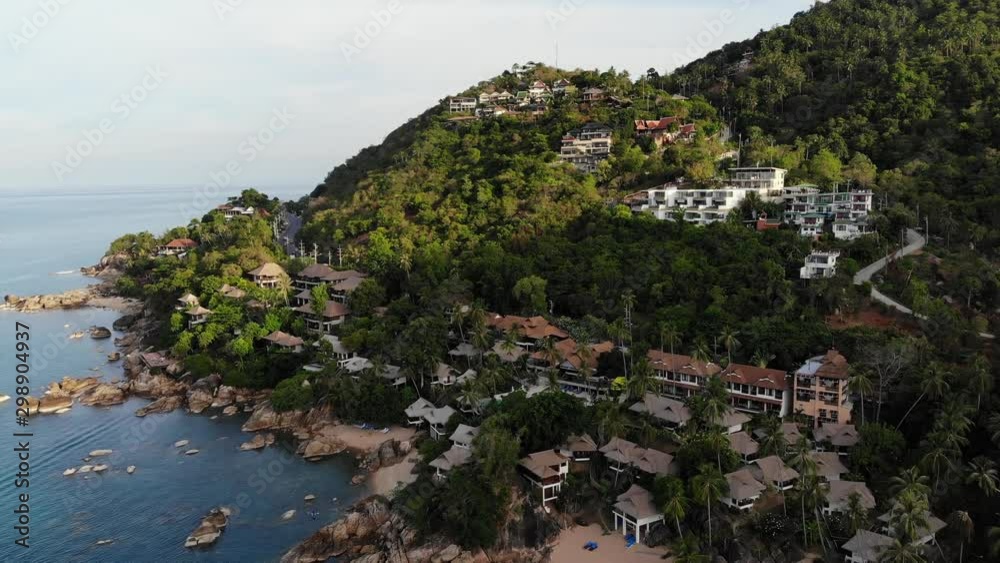 Villas on green mountain ridge. Majestic drone view of luxury villas located on green mountain range on tropical paradise island near the tiny beach. Stony shore and green jungle, volcanic Koh Samui Villas on green mountain ridge. Majestic drone view of luxury villas located on green mountain range on tropical paradise island near the tiny beach. Stony shore and green jungle, volcanic Koh Samui