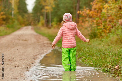 Rear view of a caucasian child girl with the arms strechted out  standing in a huge rain puddle in the forest on a rainy autumn day in October in Germany © franconiaphoto
