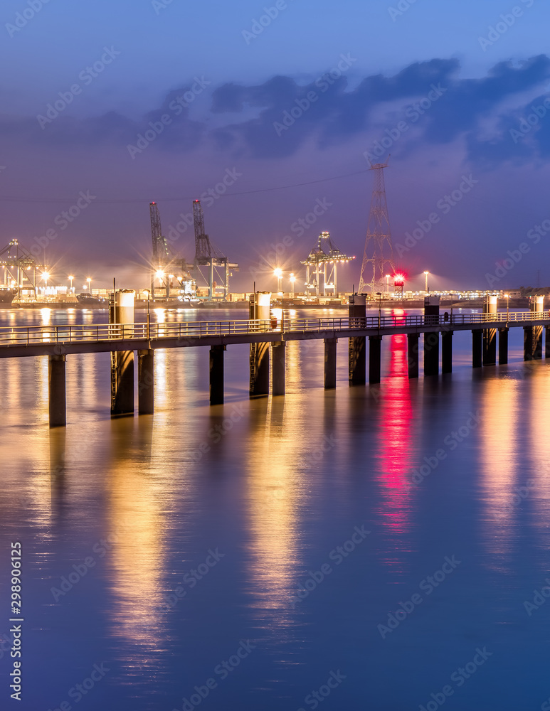 Illuminated pier in river Scheldt with container terminal on the background, Port of Antwerp, Belgium.