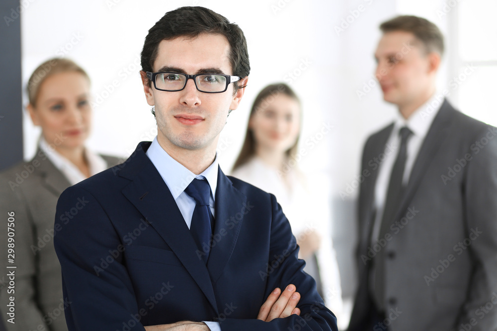 Headshot of businessman standing straight with colleagues at background in office. Group of business people discussing questions at conference or presentation. Success and business concept Headshot of businessman standing straight with colleagues at background in office. Group of business people discussing questions at conference or presentation. Success and business concept