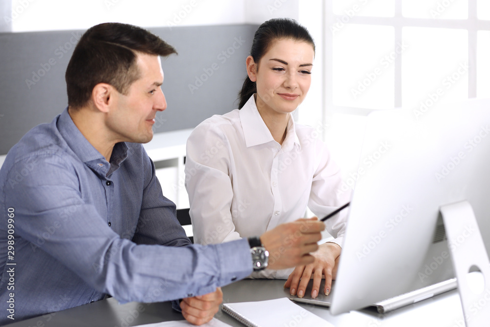 Cheerful smiling businessman and woman working with computer in modern office. Headshot at meeting or workplace. Teamwork, partnership and business concept Cheerful smiling businessman and woman working with computer in modern office. Headshot at meeting or workplace. Teamwork, partnership and business concept