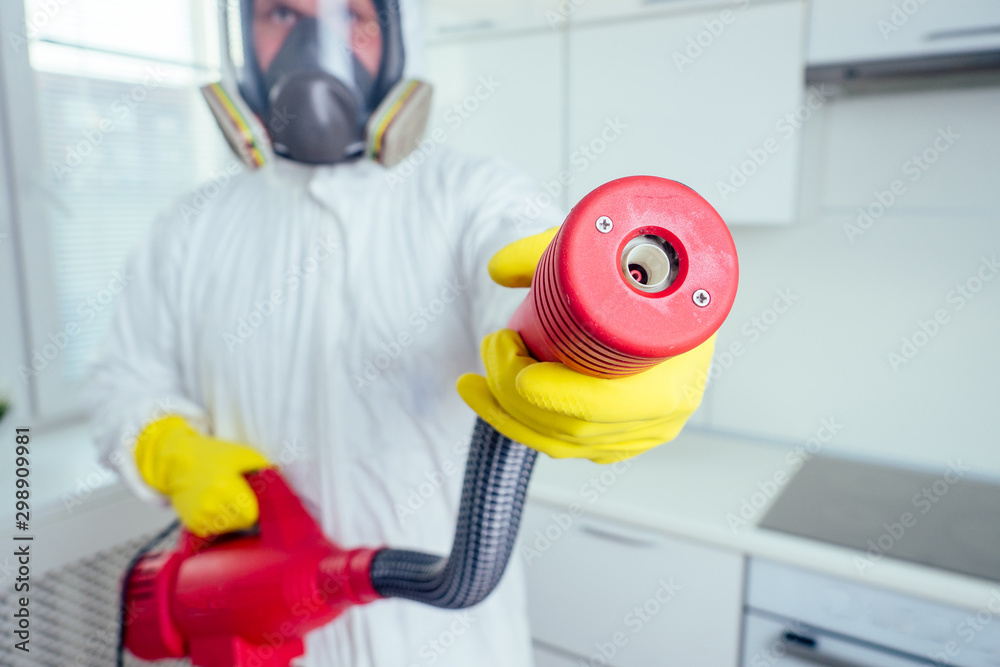 pest control worker standing with sprayer in kitchen
