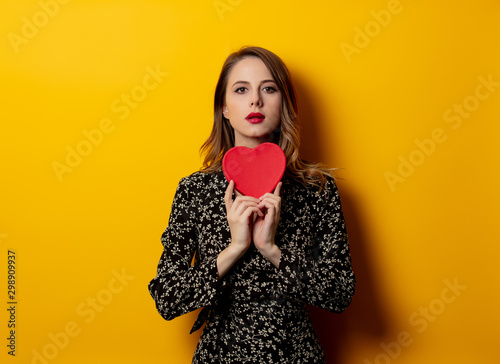 Beautiful woman with heart shape box on yellow background