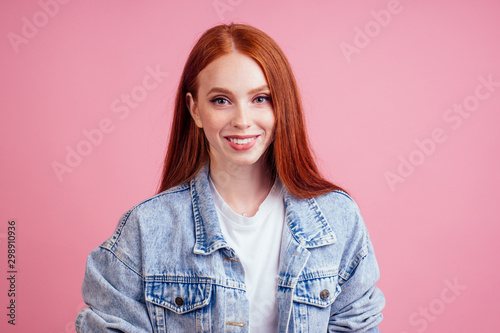 redhaired ginger woman wearing white cotton t-shirt , demin jeans jacket and small crystal jewel microdermal on neck ,smile in studio pink background