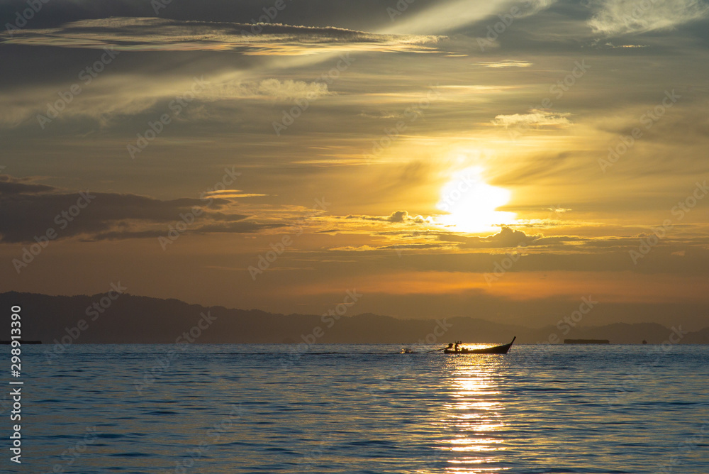 Silhouette of moving long tail boat with shadow of island  and orange light of sunrise in background. Landscape of calm sea in early morning