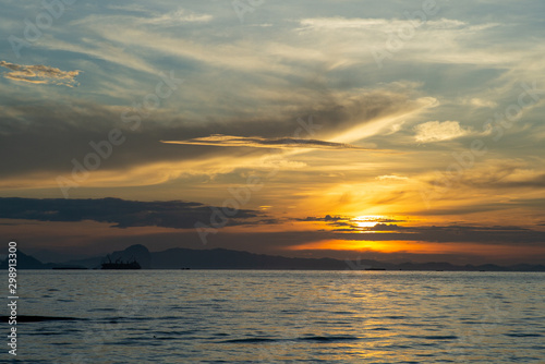 Silhouette of big ship with shadow of island  and orange light of sunrise in background