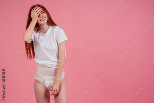 young amazed and surprised redhaired ginger woman wearing incontinence diaper in studio pink background Poster Mural XXL