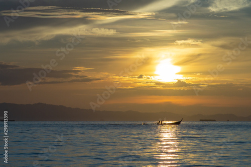 Silhouette of moving long tail boat with shadow of island  and orange light of sunrise in background. Landscape of calm sea in early morning © Phichat