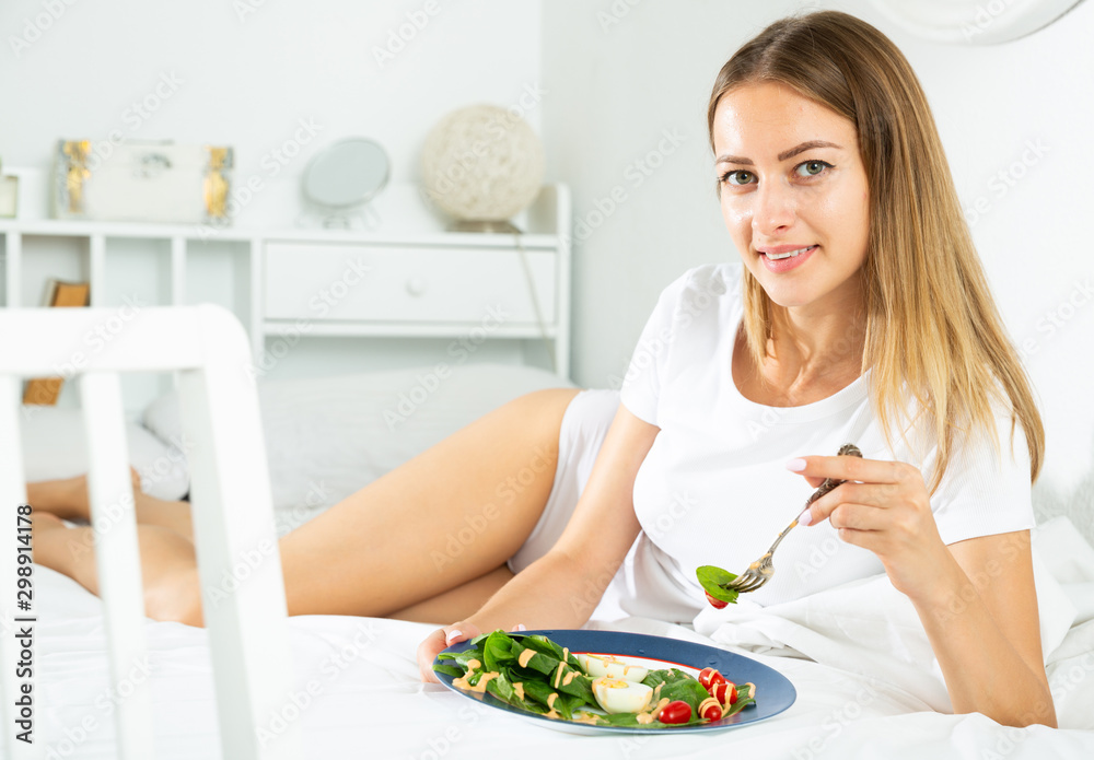 Cheerful young girl in lingerie having a salad while laying in the bed