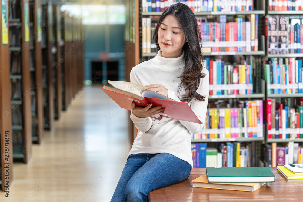 Asian young Student in casual suit reading the book in library of university or colleage on the wooden table over the book shelf background, Back to school concept Asian young Student in casual suit reading the book in library of university or colleage on the wooden table over the book shelf background, Back to school concept