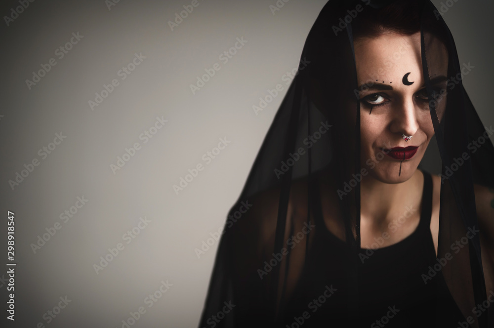 Redhead woman with a black veil on her head in a dark studio. A girl with an earring in her nose smiles slyly. Witch Makeup. Halloween costume. Redhead woman with a black veil on her head in a dark studio. A girl with an earring in her nose smiles slyly. Witch Makeup. Halloween costume.