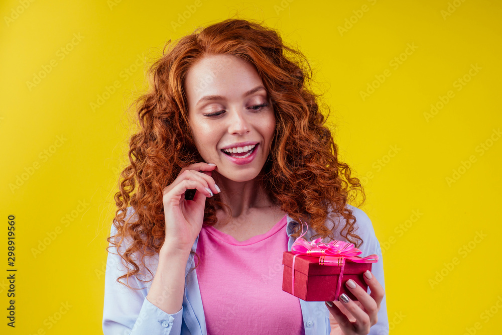 redhair curly ginger woman holding gift box in studio yellow background.mother's day and eighth of marchor St. Valentine's Day concept