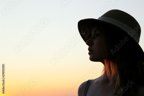 Blurred image of a young girl wearing a hat and looking to the side, beautiful sky bakground. People, travel concept.