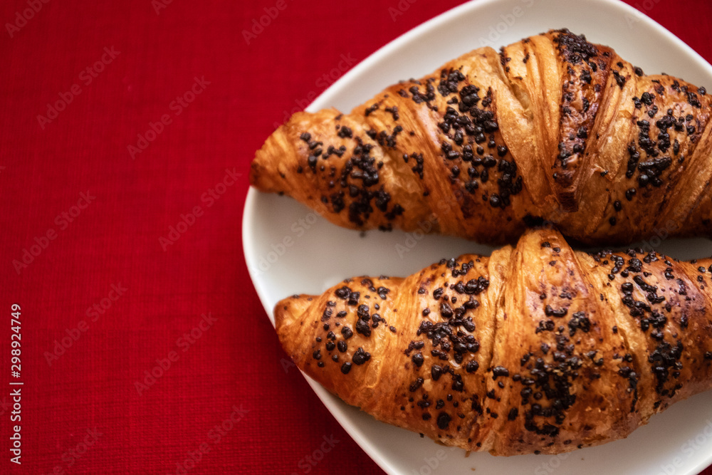 Two delicious croissant with chocolate chips in a white plate on a bright red background, top view