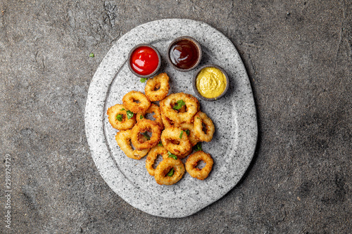 Fried squid rings on gray stone plate with sauces. Gray concrete background