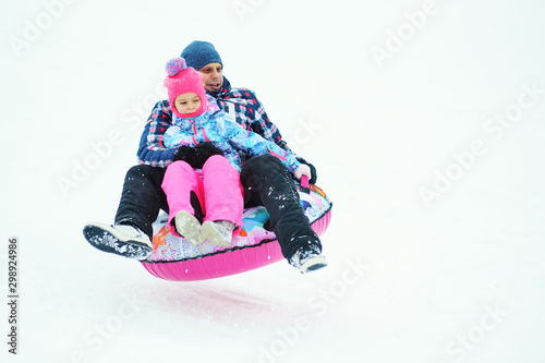 dad and daughter in ski suits ride on tubing on a snowy hill. photo