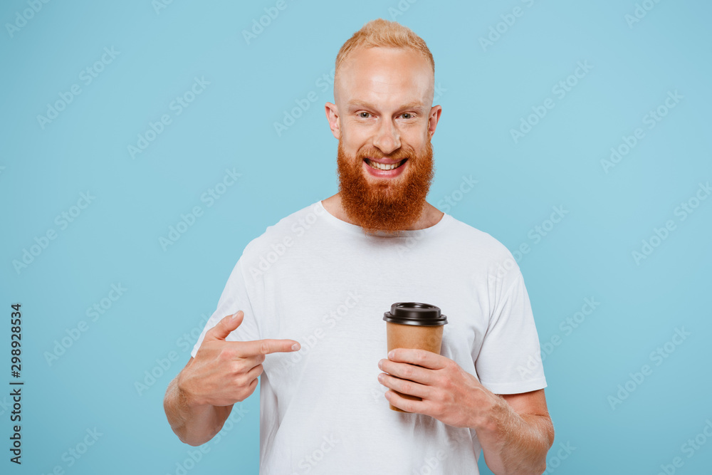 happy bearded man in t-shirt pointing at coffee to go, isolated on blue happy bearded man in t-shirt pointing at coffee to go, isolated on blue