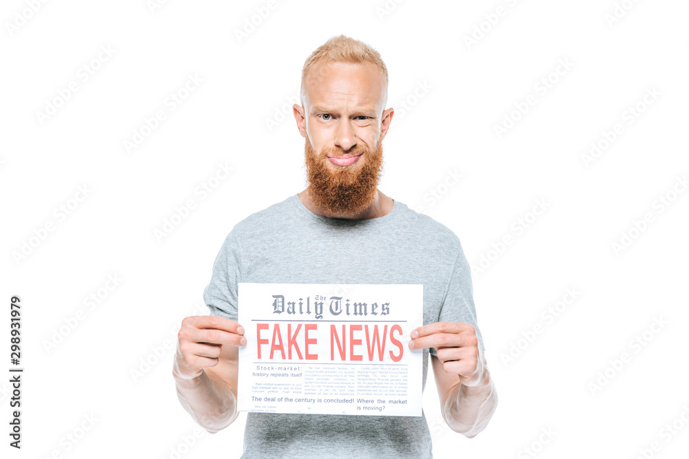 skeptical bearded man showing newspaper with fake news, isolated on white