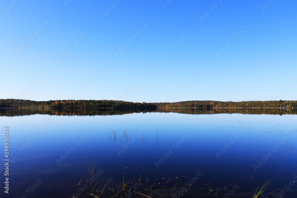 View of shoreline and beach around a lake in autumn, Nova Scotia, Canada. Trees in fall colors. Reflection in the water's surface. View of shoreline and beach around a lake in autumn, Nova Scotia, Canada. Trees in fall colors. Reflection in the water's surface.