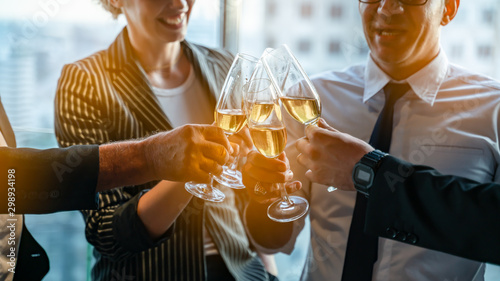 Toasting to success concept.Group of business people toast with champagne and smiling while standing close to each in bar.Friends clinking and toasting with glasses of champagne in lounge.