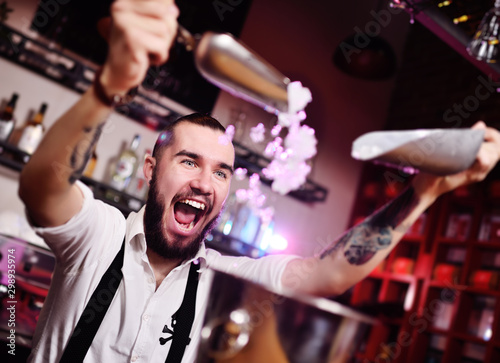 a handsome bearded bartender in a white shirt pours ice for cocktails and screams happily against the bar at a nightclub party
