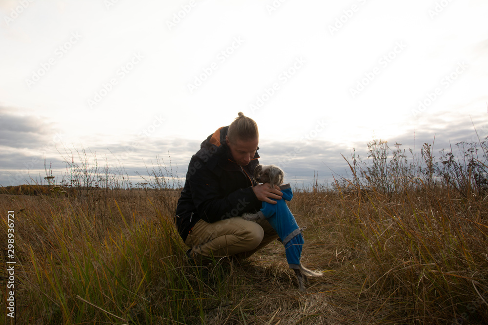 A middle-aged man walks with a dog breed Chinese Hairless Crested Dog on nature in autumn afternoon. A middle-aged man walks with a dog breed Chinese Hairless Crested Dog on nature in autumn afternoon.